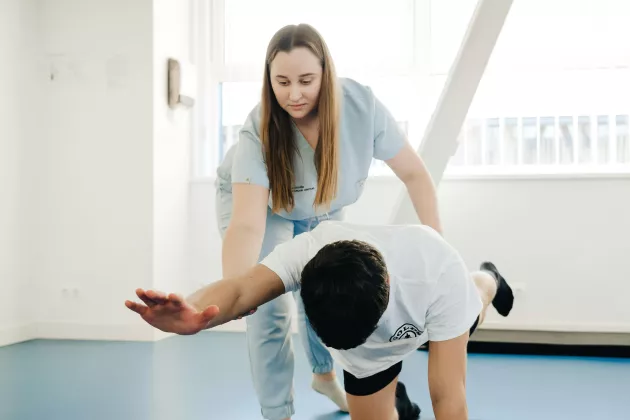 En person i vårdkläder som instruerar en person som står på alla fyra och utför träningsövningar